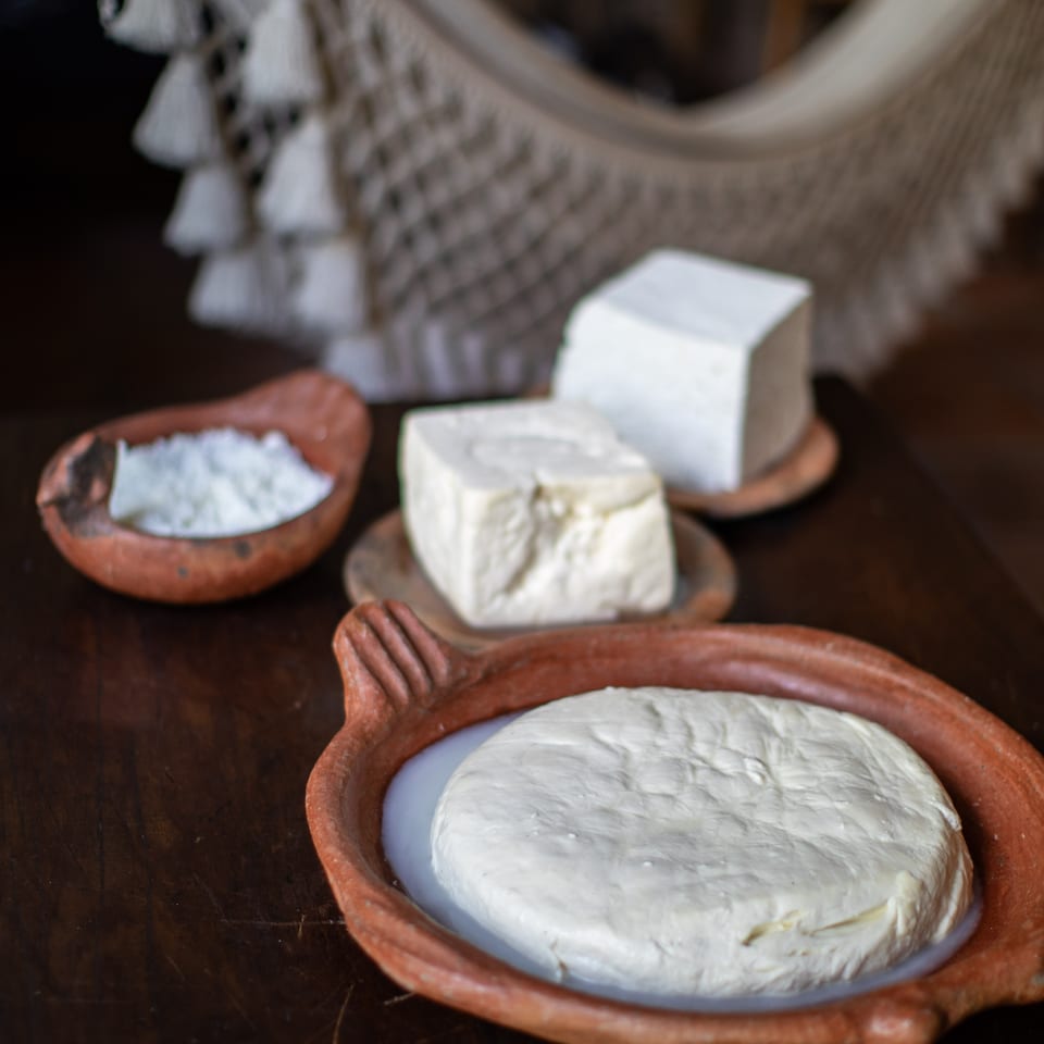 Traditional white cheeses displayed in rustic clay bowls on a dark wooden table.